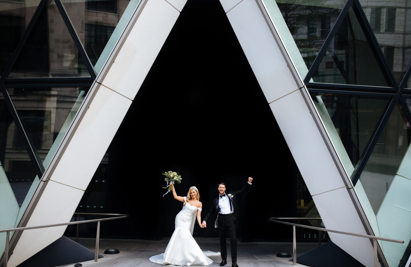 bride and groom throwing their hands up in joy in front of the gherkin