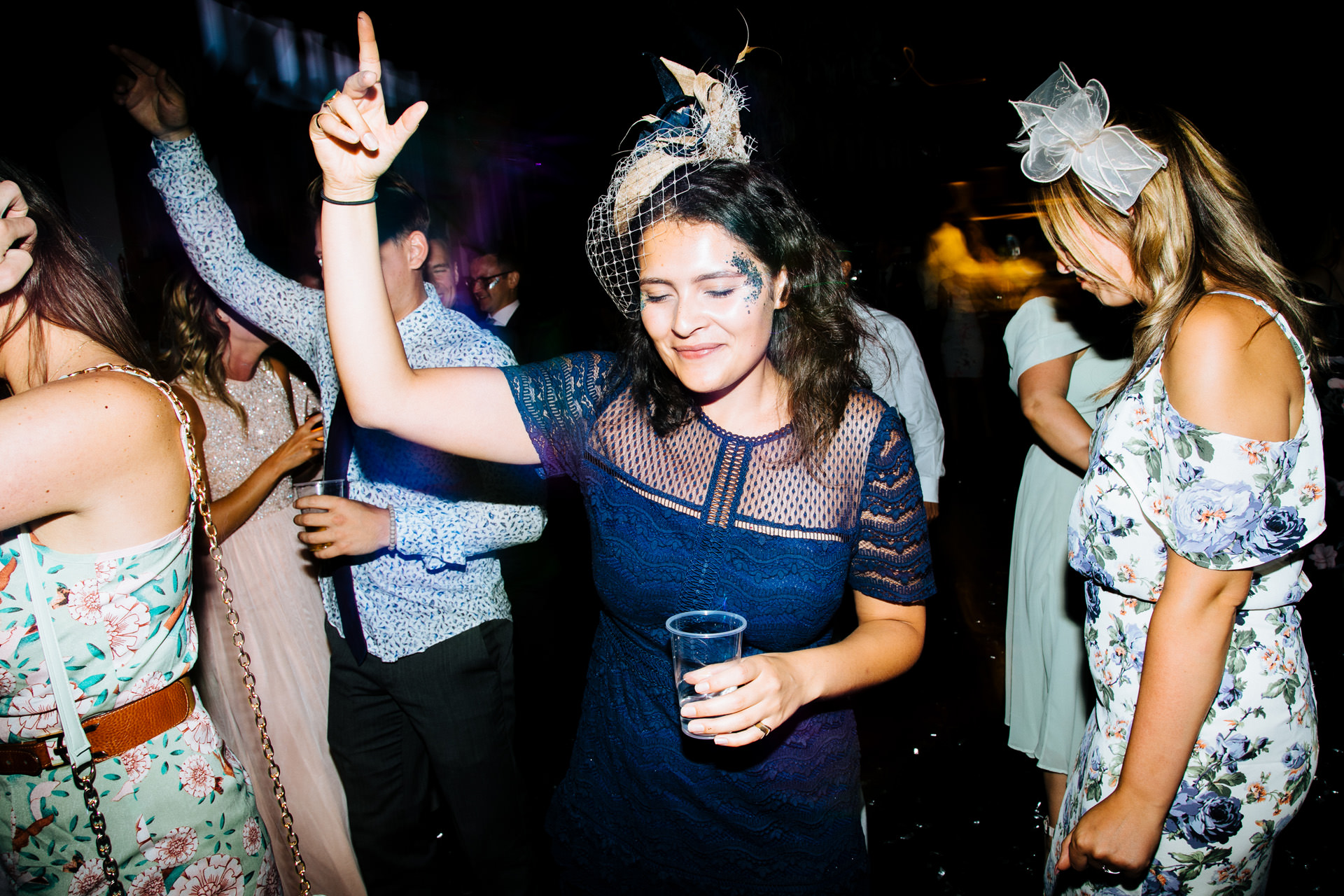 lady in navy blue dress and fascinator wearing glitter on her face partying