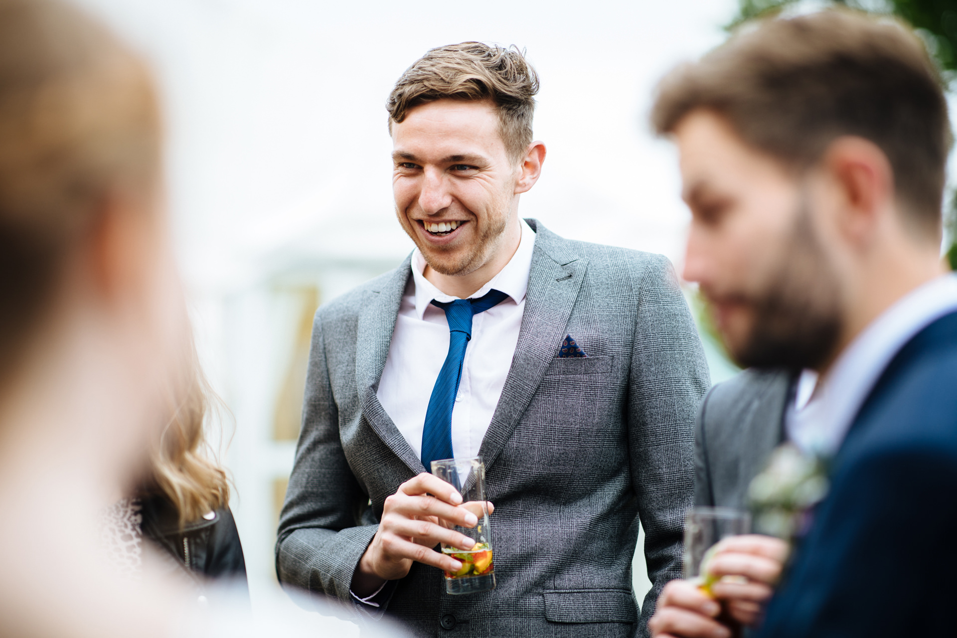 wedding guest in grey suit and teal tie laughing