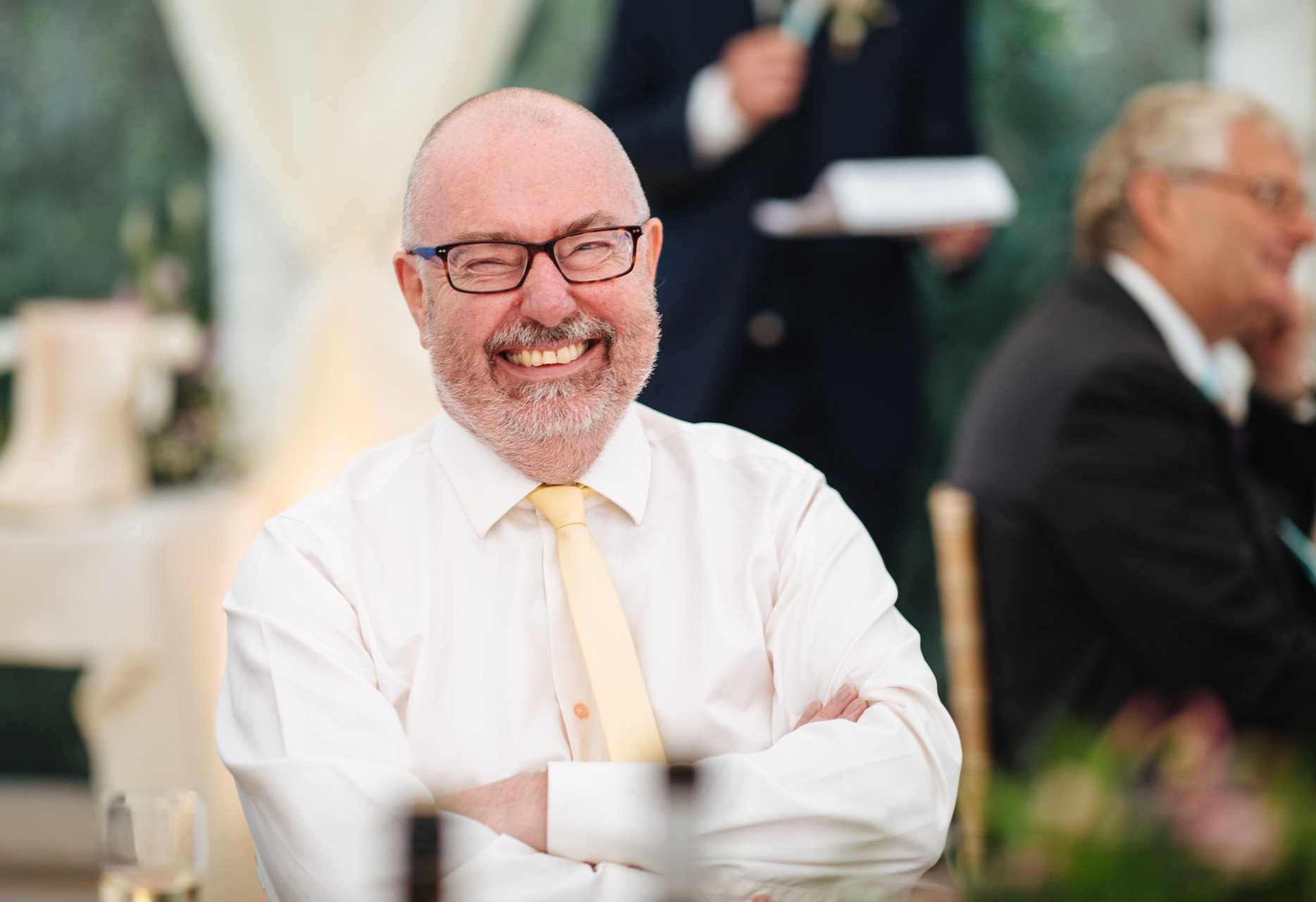 wedding guest with yellow tie and glasses laughing at wedding speech